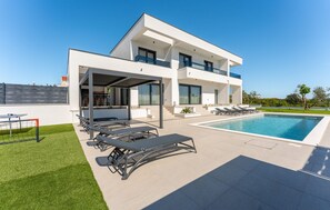 Ein modernes, zweistöckiges Haus mit Swimmingpool, Außenbereich zum Sitzen und einer überdachten Terrasse.