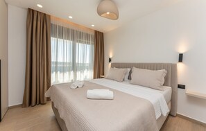 Ein modernes Hotelzimmer mit einem großen Bett, einem Flachbildfernseher und einem Fenster mit transparenten Vorhängen.