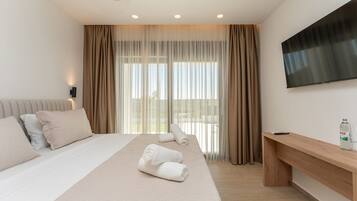 A hotel room with a bed, a TV, a desk, and a window with curtains.