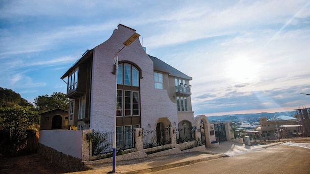 Una casa moderna de dos pisos con ventanas amplias, un balcón y un muro de piedra.