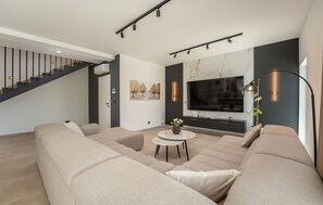 Ein modernes Wohnzimmer mit einer großen Couch, einem kleinen Tisch mit einer Vase, einem Flachbildfernseher und einer Treppe.