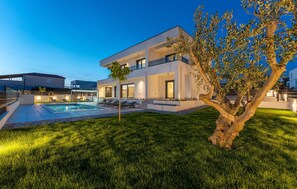 Ein modernes, zweistöckiges Haus mit Pool, gepflegtem Rasen und einem Baum.
