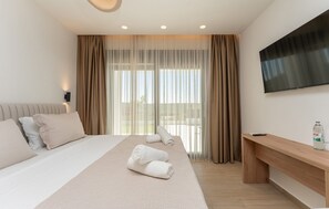 Ein Hotelzimmer mit Bett, Fernseher, Schreibtisch und einem fenster mit Vorhängen.