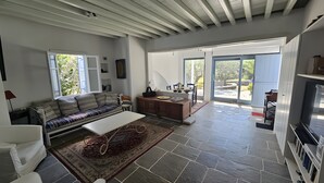 Ein modernes Interieur mit einer Couch, Esstisch, Küchenzeile und großen Schiebeglasfenstern, die zu einem Außenbereich führen.