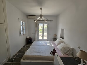 Un dormitorio con una cama, una mesita de noche, una lámpara, una ventana y un aire acondicionado.