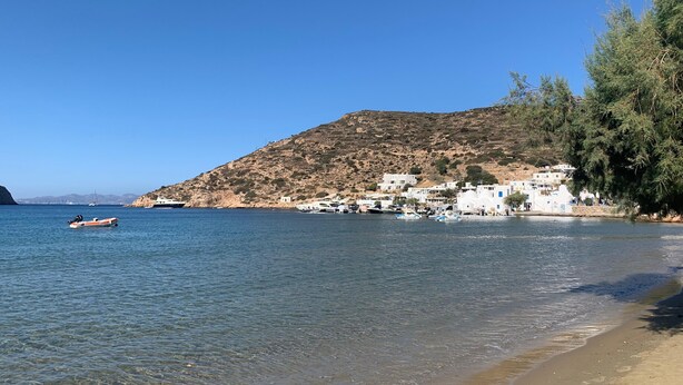 Eine Küstenlandschaft mit Strand, klarem Wasser, Booten und Gebäuden an einem Hang.