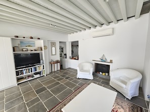 Una sala de estar con un televisor de pantalla plana, estanterías, chimenea, un sillón blanco y una alfombra estampada.