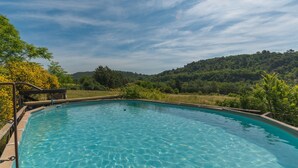 Ein klares Schwimmbecken mit Holzterrasse und Blick auf einen bewaldeten Hang.