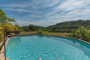 Ein klares Schwimmbecken mit Holzterrasse und Blick auf einen bewaldeten Hang.