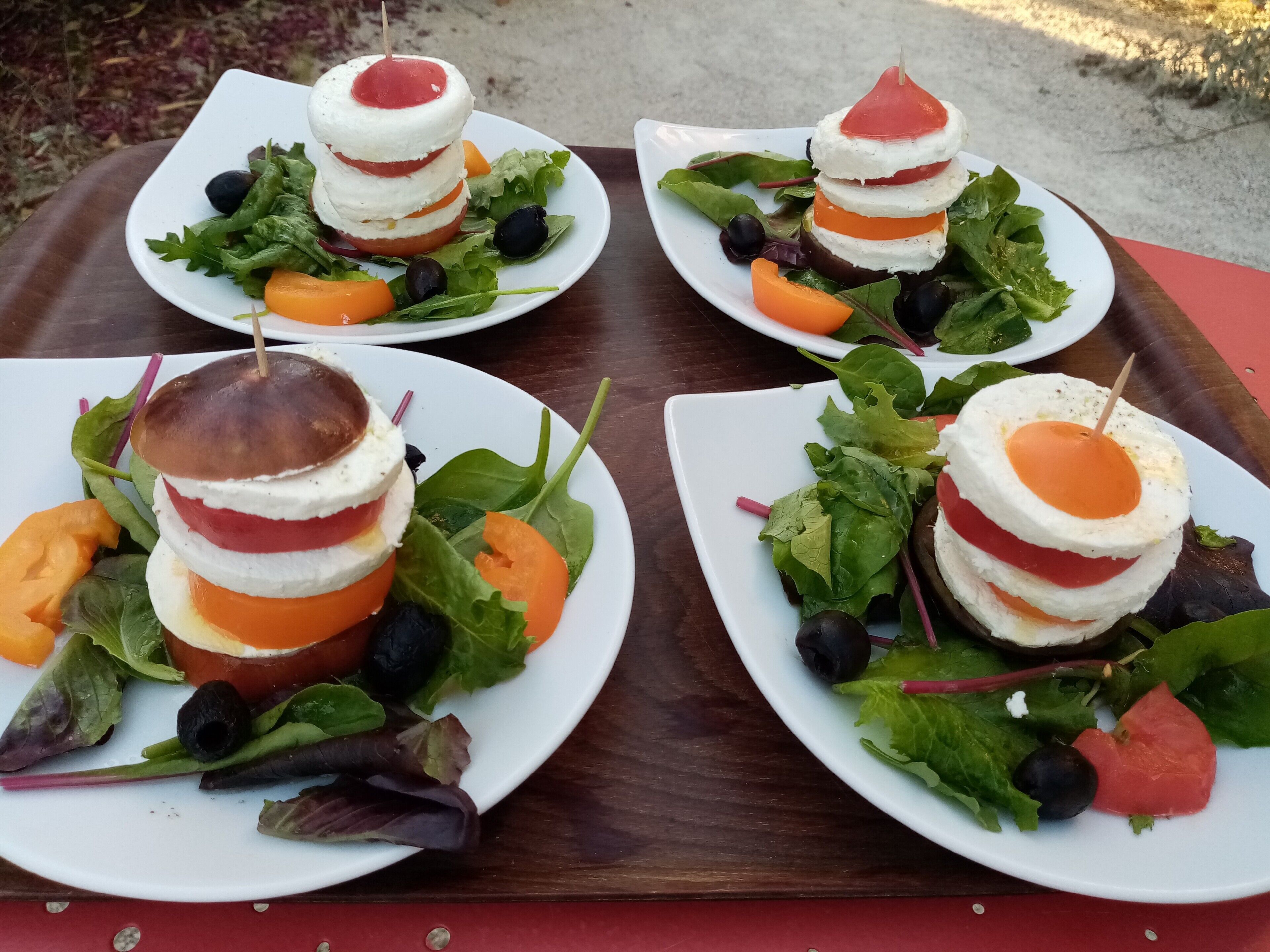 Four plates of food with a layered sandwich and salad, arranged on a wooden tray.