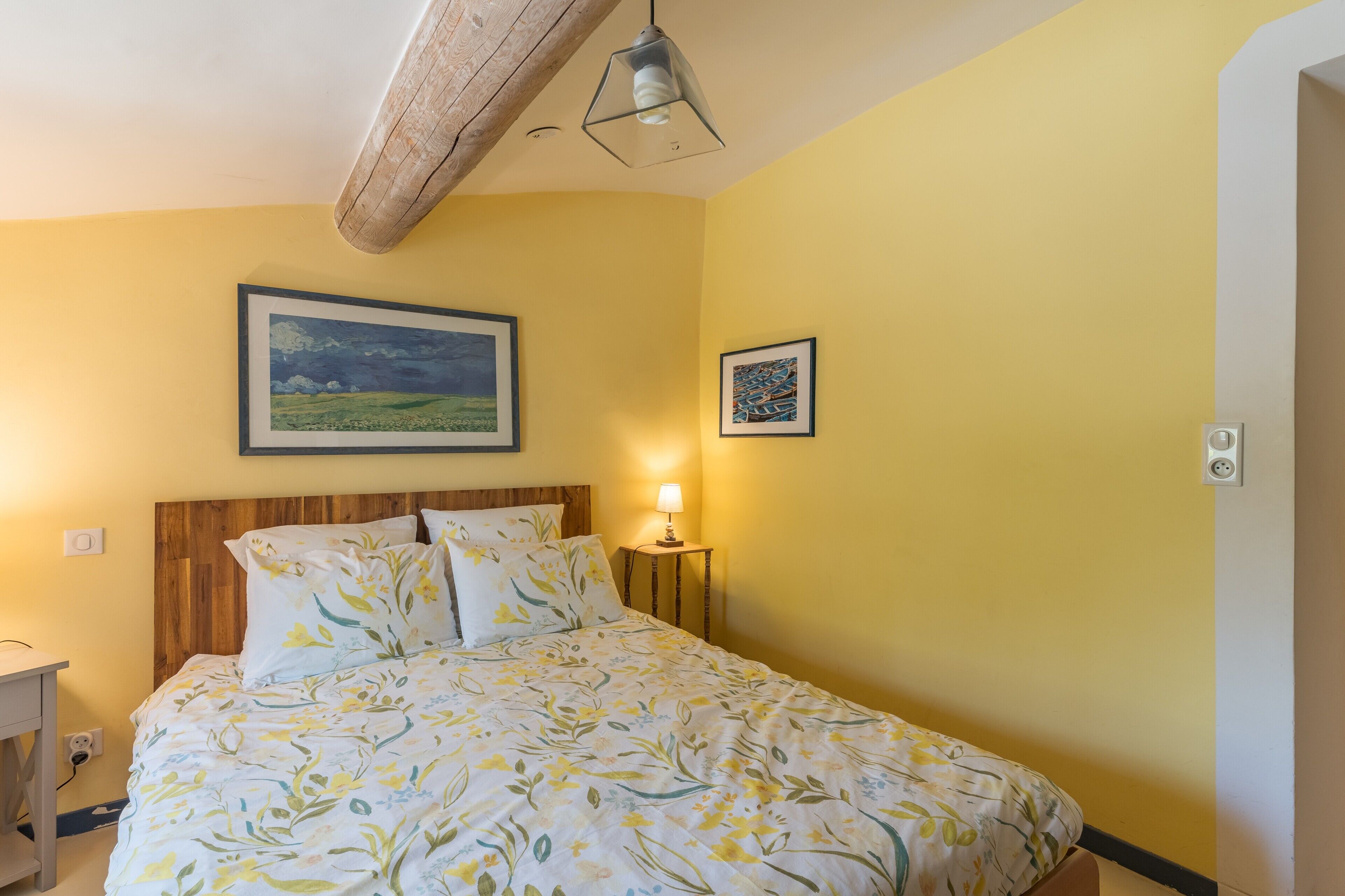 Une chambre à coucher avec un lit, une table de chevet, une lampe et deux tableaux encadrés accrochés au mur.
