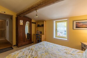 Une chambre à coucher avec un lit, une armoire en bois, un bureau avec des livres, une chaise, une fenêtre donnant sur un paysage agréable et un luminaire au plafond.