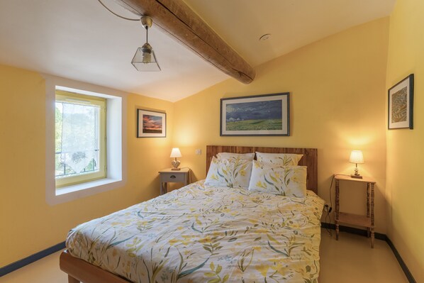 Une chambre à coucher avec un lit, deux tables de chevet avec des lampes, une fenêtre et deux tableaux encadrés accrochés au mur.