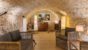 An arched stone interior with a wooden floor, wicker furniture, a small table, a bicycle, and a kitchen area visible through an archway. - Ma maison de loin - Saturnin Room (Apt)