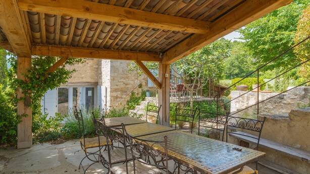 An outdoor patio with a wooden pergola, a metal table with chairs, and a stone wall in the background. - Ma maison de loin - Saturnin Room (Apt)