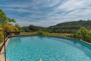A clear swimming pool with a wooden deck and a view of a forested hillside. - Ma maison de loin - Rustrel Room - 1 (Apt)