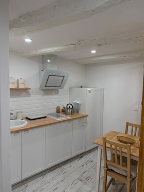 Eine Küche mit weißen Schränken, einer Holz Arbeitsplatte, einem Wasserkocher, einer Kaffeemaschine und einem kleinen Tisch mit einem Korb.
