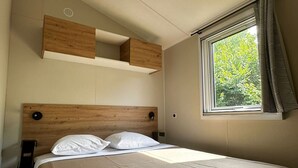 Quarto com cabeceira de madeira, cama com roupa de cama branca, janela com cortinas e prateleira embutida acima da cama.