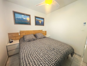 Ein Schlafzimmer mit einem Bett, Nachttischen, einem Deckenventilator und zwei gerahmten Bildern an der Wand.