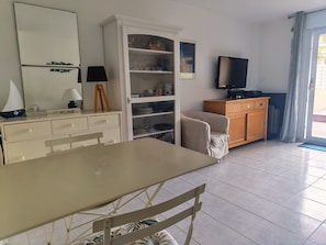 Ein Zimmer mit einem Esstisch, einer weißen Schrank mit Regalen, einem Fernseher und einem Sessel.