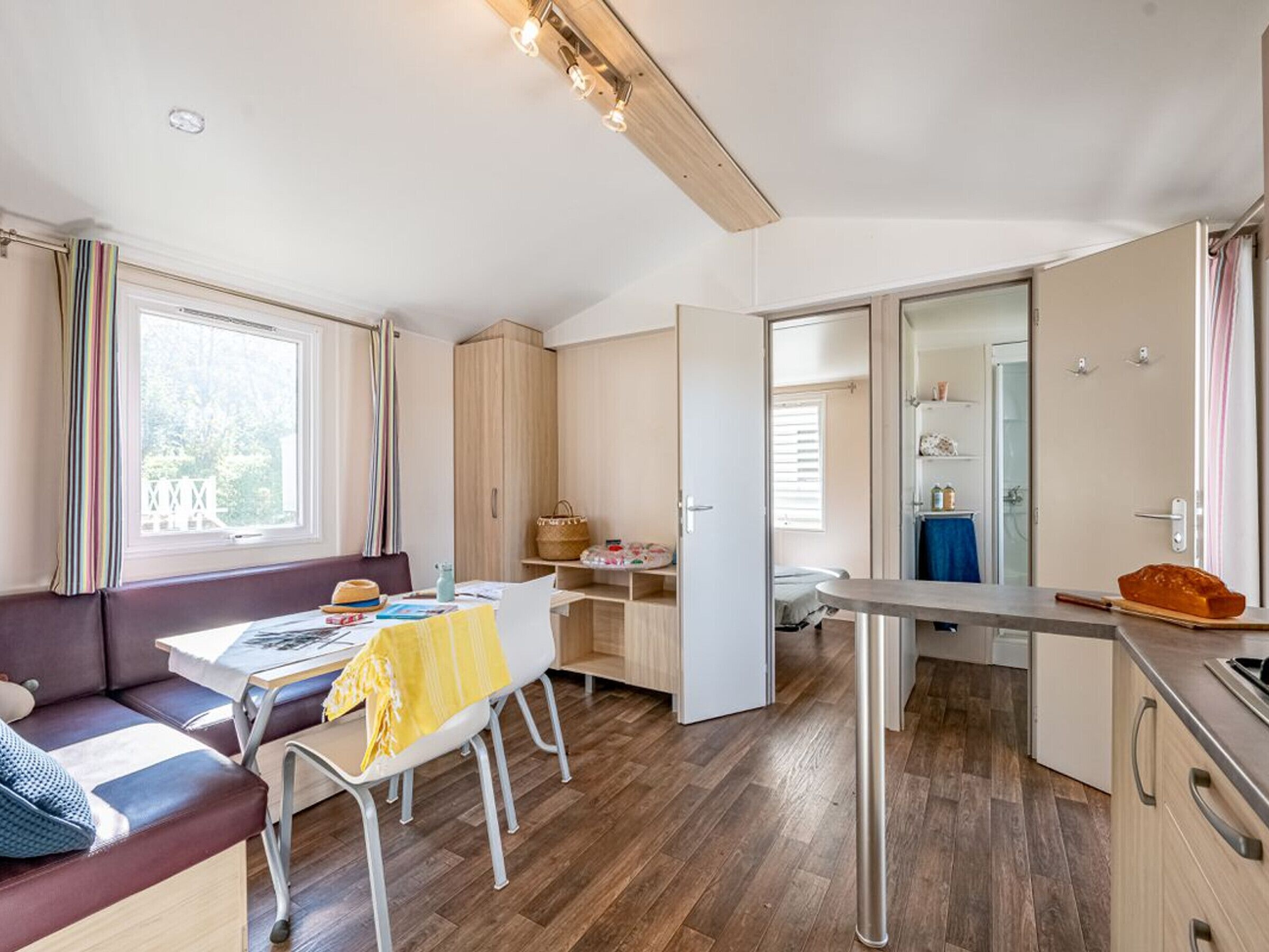 A modern, well-lit room with a sofa, dining table, and kitchenette.