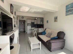 Un salon moderne avec un canapé, un téléviseur et un coin repas équipé de chaises.