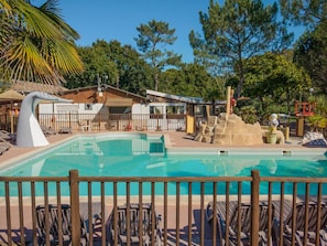 A pool area with lounge chairs, a lifeguard tower, and a building with a thatched roof. - Mobile home, pets welcome - 4 guests (Grayan-et-l'Hôpital)