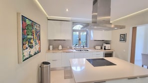 A modern kitchen with white cabinets, a stainless steel range hood, a window with a view, and a colorful painting on the wall. - Algarve Stunning Villa by Homing (Faro)