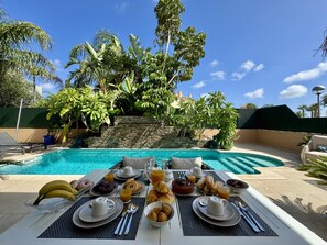 A breakfast setup with a pool and tropical plants in the background. - Algarve Stunning Villa by Homing (Faro)