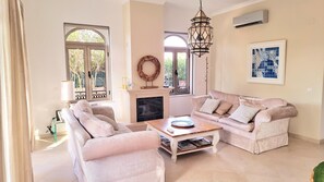 A living room with a fireplace, two sofas, a coffee table, and a decorative wall piece. - Algarve Stunning Villa by Homing (Faro)