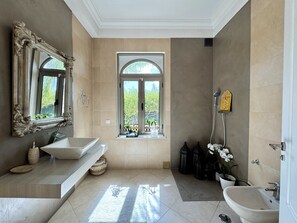 A bathroom with a large mirror, a freestanding sink, a bathtub, and a window with a view of greenery.