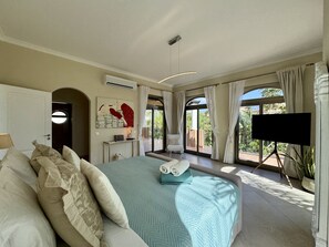 A spacious bedroom with a large bed, a flat-screen TV, and a view of the outdoors.