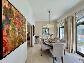 Un coin repas avec une table dressée pour quatre personnes, un lustre et un grand tableau abstrait accroché au mur.