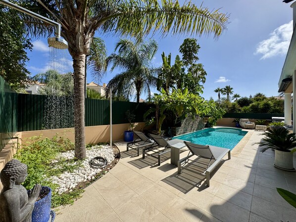 A swimming pool with lounge chairs, a statue, and a green fence.