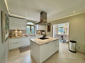 A modern kitchen with a central island, built-in appliances, and a dining area with a view. - Algarve Stunning Villa by Homing (Faro)