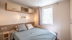 Un dormitorio con cama, mesitas de noche, estante en la pared y ventana con cortinas.