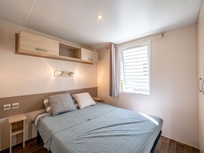 Ein Schlafzimmer mit einem Bett, Nachttischen, einem Wandregal und einem Fenster mit Vorhängen.