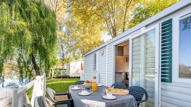 Una terraza con una mesa lista para dos, sillas y vistas a una casa móvil.