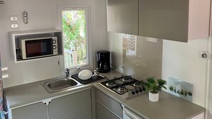 Eine kompakte Küche mit Mikrowelle, Spüle, Herd und einem Fenster mit Blick auf Grünfläche.