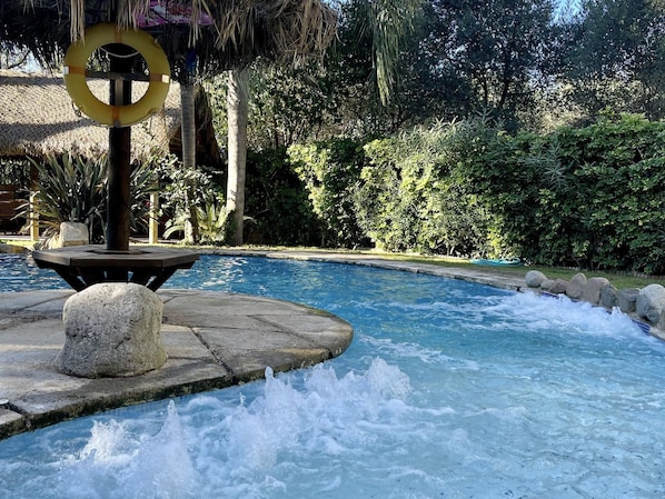 A swimming pool with a water fountain feature, surrounded by lush greenery and a thatched structure. - Spacious apartment - 8 guests, heart of Riudoms (Riudoms)