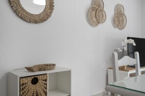 Een witte kamer met een geweven mand op een witte kast, een televisie op een houten standaard, en een witte stoel.