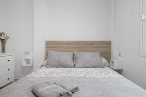 Een keurig opgemaakt slaapkamer met een houten hoofdbord, een witte nachtkastje, een ladeunit en een bed met een bedsprei met patroon en twee kussens.