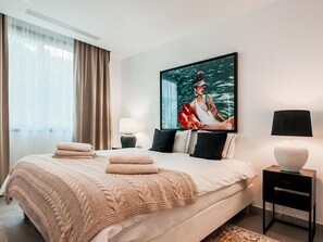 Ein modernes Hotelzimmer mit einem großen Bett, einem Flachbildfernseher, einem Nachttisch mit Lampe und Blick ins Freie.