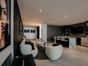 Ein modernes Wohnzimmer mit einer Couch, Sesseln, einem Essbereich und einer Küche mit Fernseher.