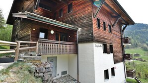 Puinen alppimaja, jossa on parveke, kiviporras ja näkymä ympäröivään maisemaan.