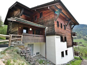 Eine Holzhütte mit Balkon, Steinstufen und Blick auf die umliegende Landschaft.