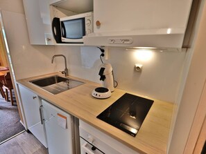 Eine kleine Küche mit Spüle, Mikrowelle, Kaffeemaschine und Induktionskochfeld.