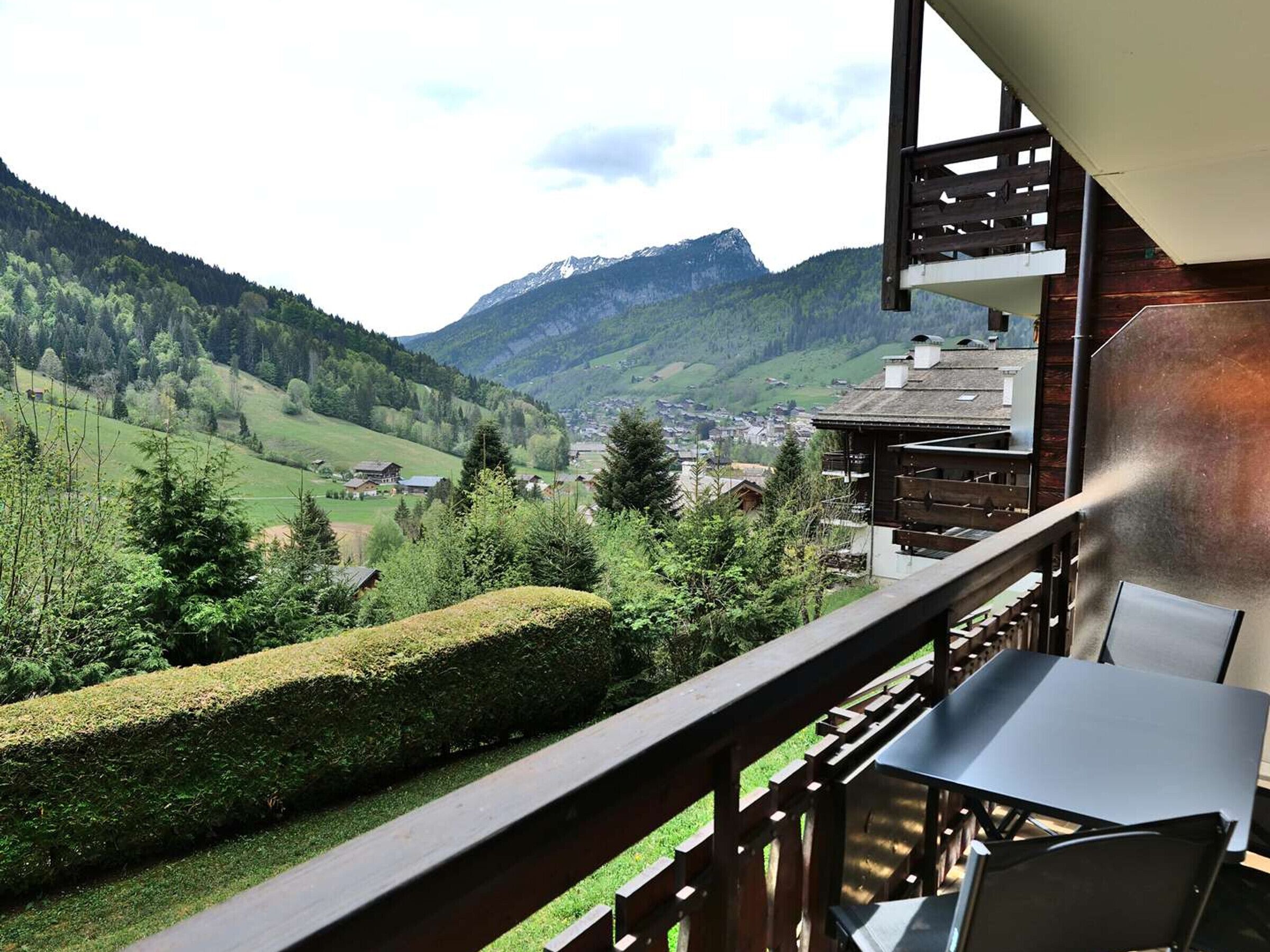 A balcony with a view of a mountainous landscape, a wooden deck, and a table with chairs.