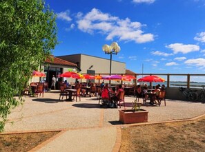 Ein Patio im Freien mit Tischen, Stühlen, Sonnenschirmen und Blick auf das Wasser.