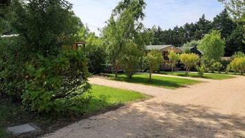 Une allée de gravier mène à un bâtiment entouré d’arbres et de verdure.